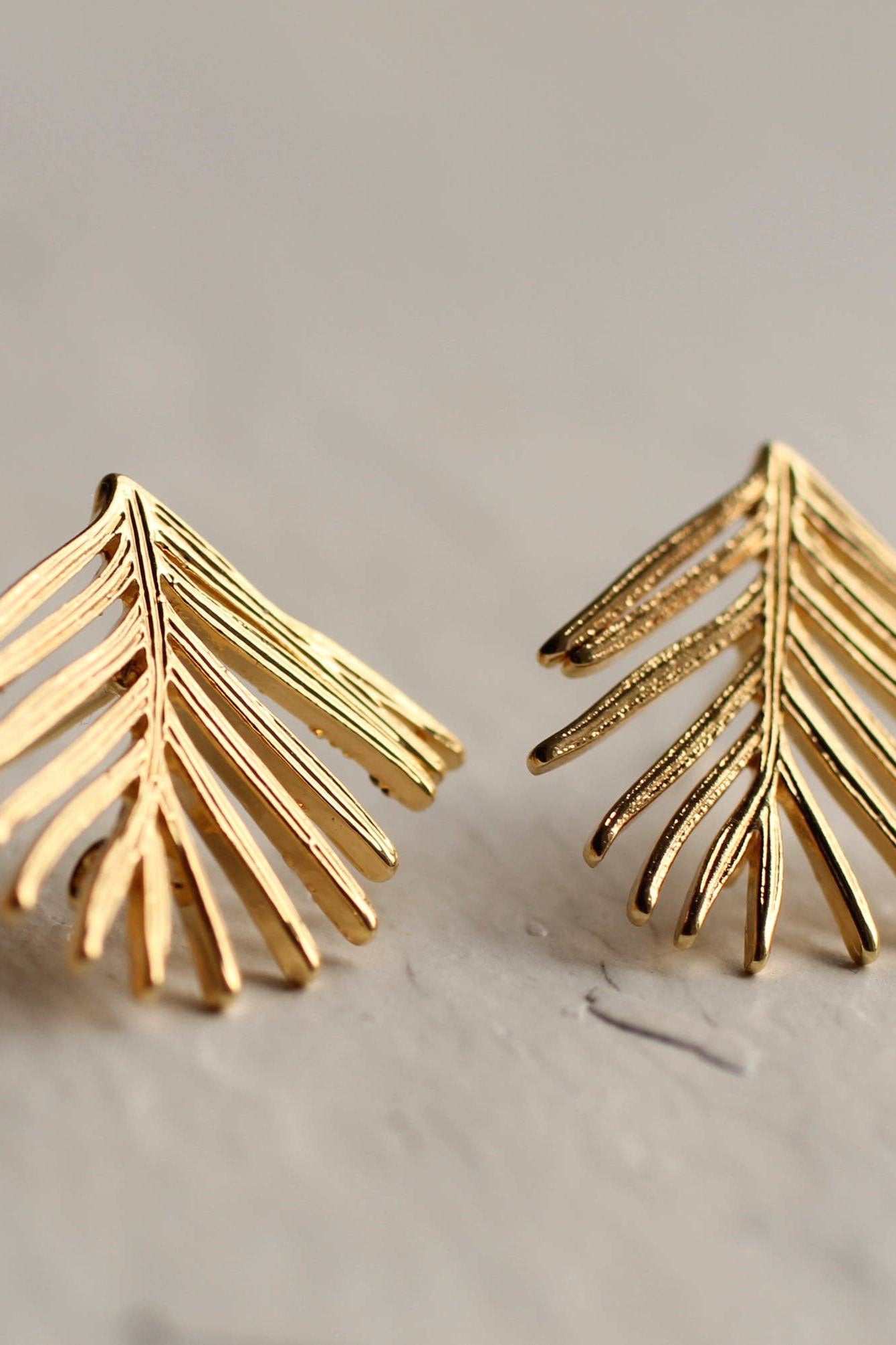 Gold leaf-shaped earrings on a light gray background