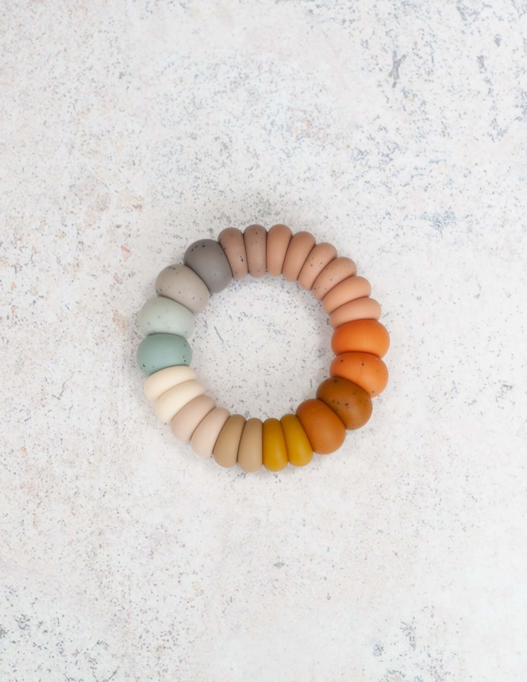 A silicone teething ring with a variety of earthy tones designed for babies.