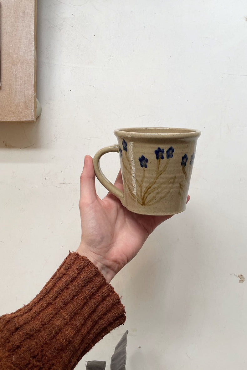 Hand holding a ceramic mug with floral designs against a plain background