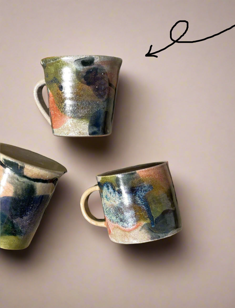 Three ceramic mugs with multicolored glaze on a concrete surface